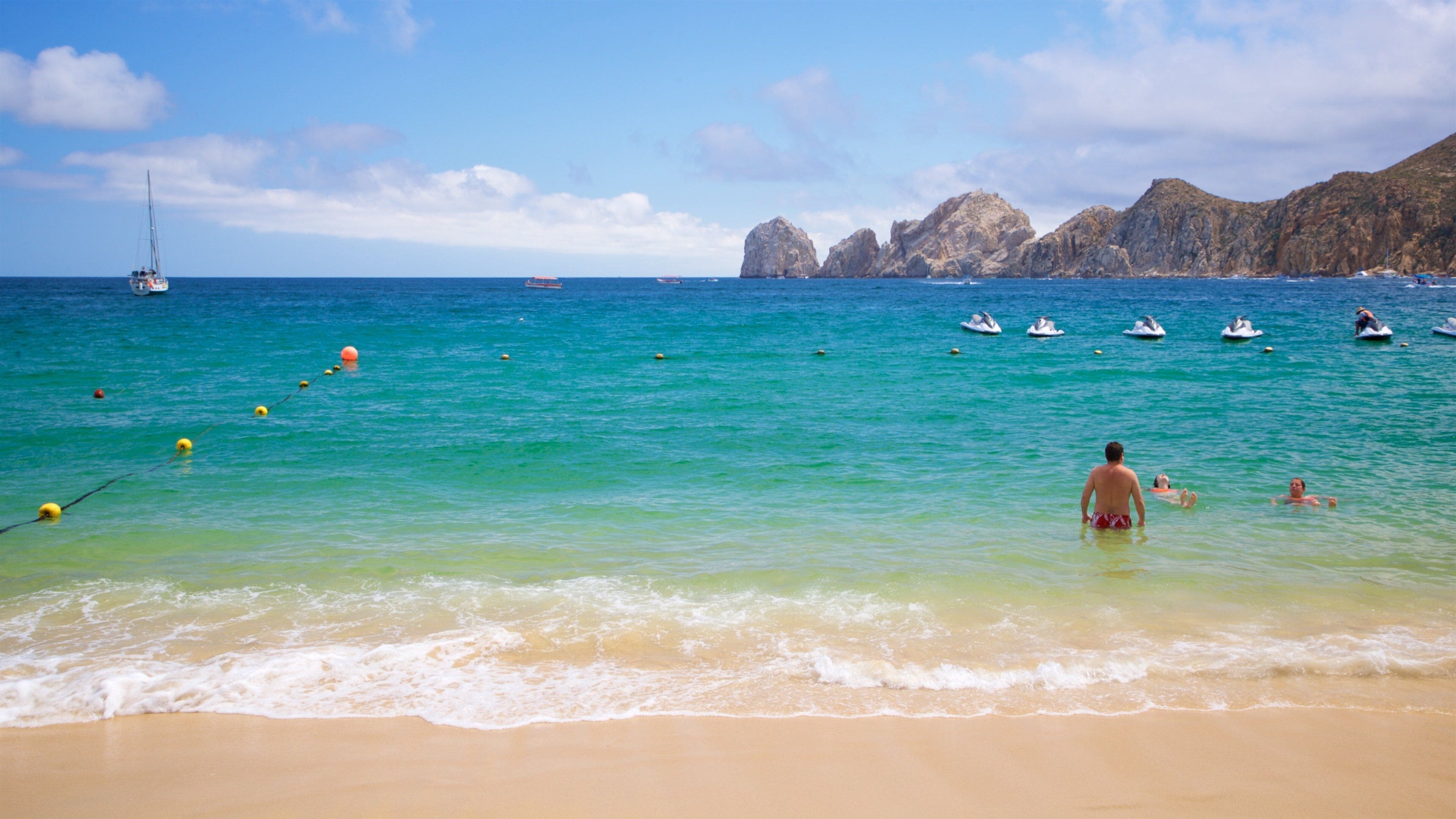 Una spiaggia con acque turchesi cristalline, una barca a vela e scogliere rocciose sullo sfondo.