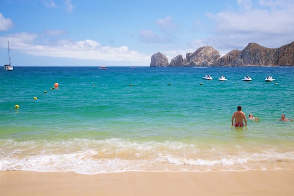 Uma praia com águas turquesa cristalinas, um veleiro e falésias rochosas ao fundo.