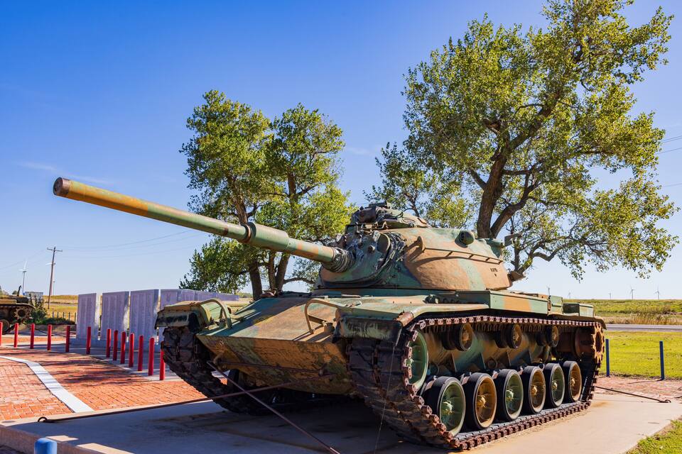 Un tanque militar exhibido al aire libre, con árboles y un cielo despejado de fondo.