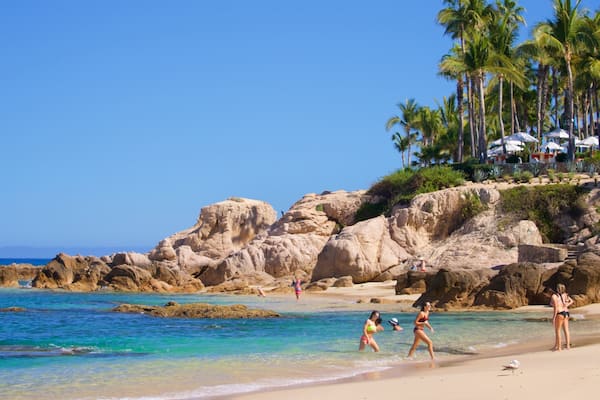 Uma praia com águas turquesa cristalinas, formações rochosas e palmeiras.
