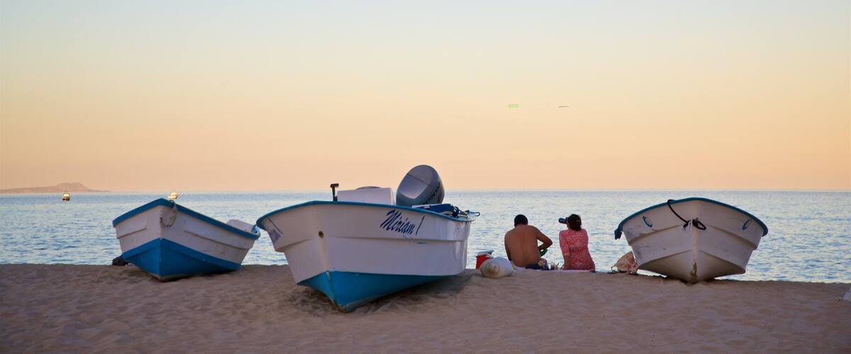 Three boats on a sandy beach with a calm sea and a clear sky.