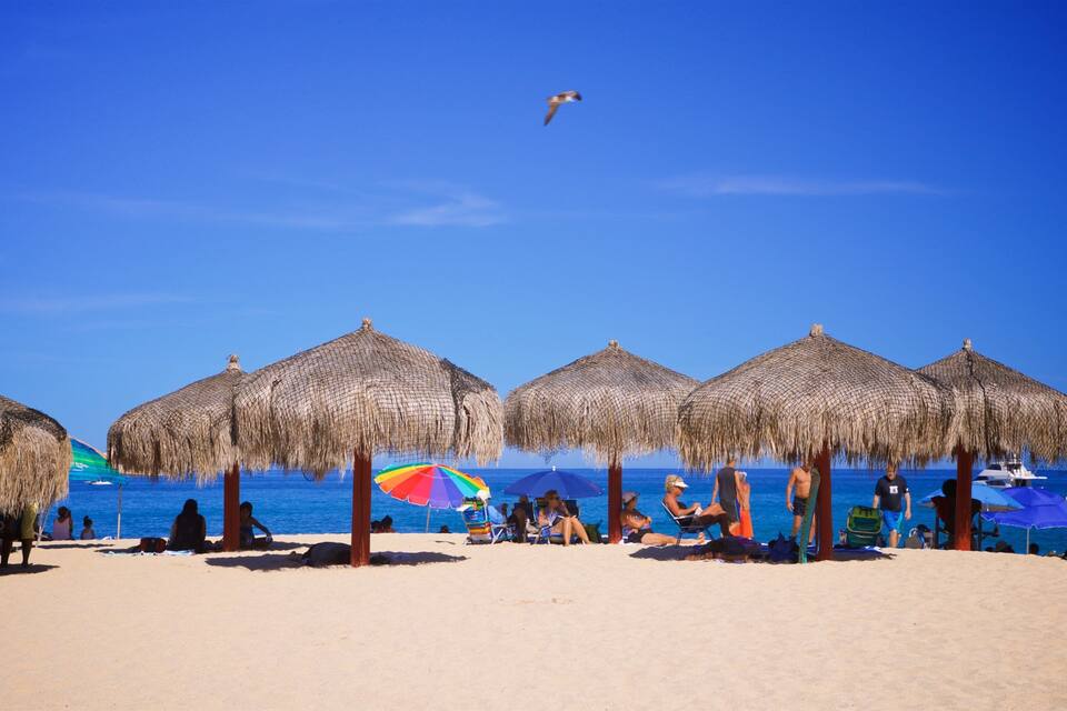 Una playa con sombrillas de paja y gente relajándose.