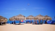 Een strand met rieten parasols en mensen die ontspannen.