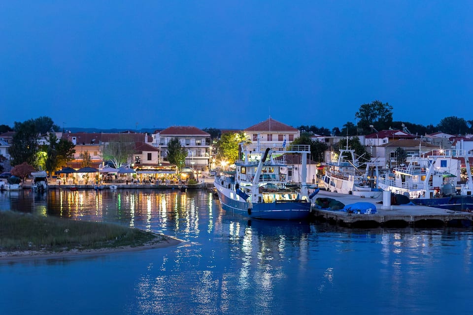 Un puerto deportivo con barcos amarrados, edificios frente al agua y un cielo sereno al atardecer.