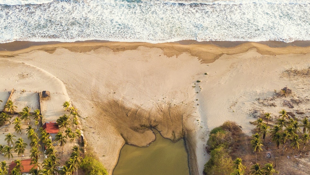 Eine Luftaufnahme einer Küstenlandschaft mit Strand, einem kleinen Gewässer und Palmen.
