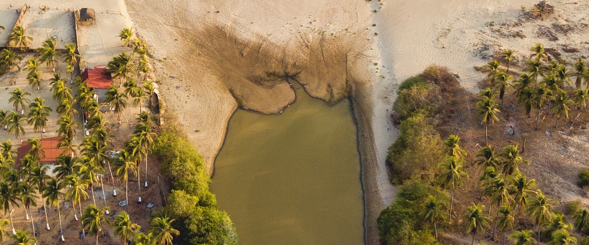 Ett flygbildsfoto av ett kustområde med en strand, en liten sjö eller damm och palmer.