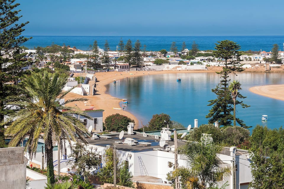 A coastal town with a beach, calm sea, and surrounding greenery.