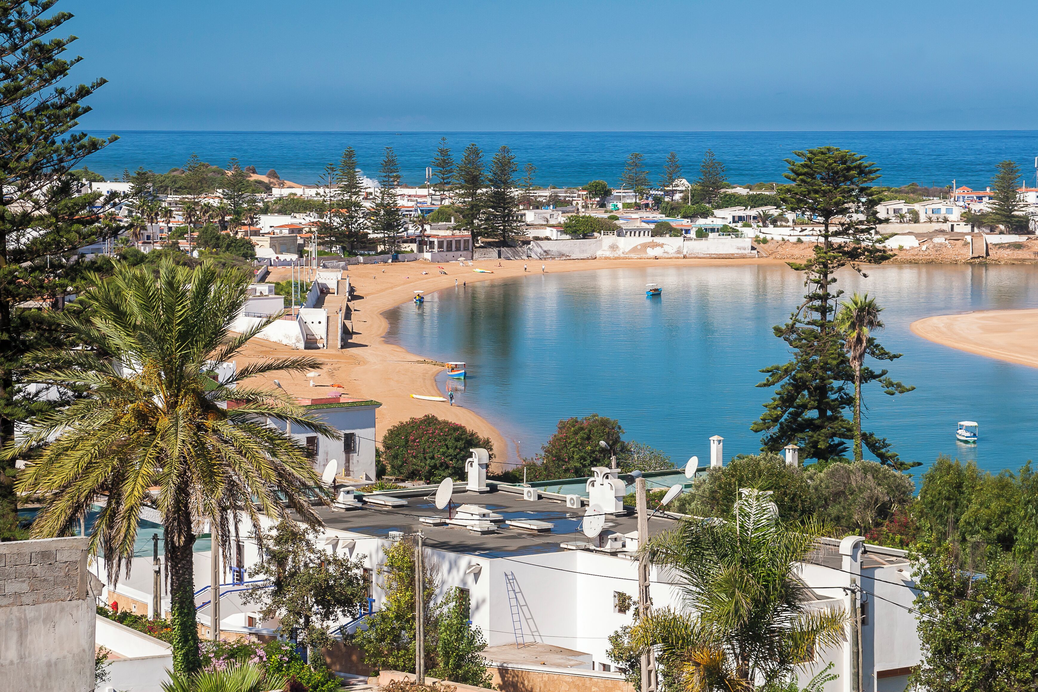 A coastal town with a beach, calm sea, and surrounding greenery.