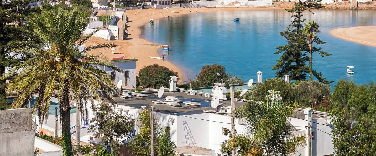 A coastal town with a beach, calm sea, and surrounding greenery.