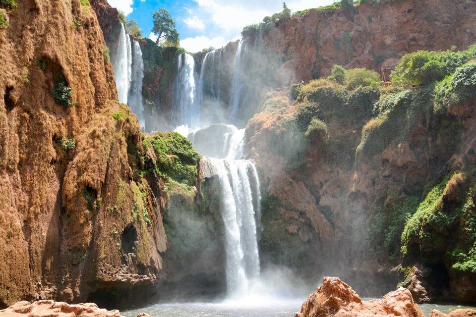 A multi-tiered waterfall surrounded by rugged cliffs and lush greenery.