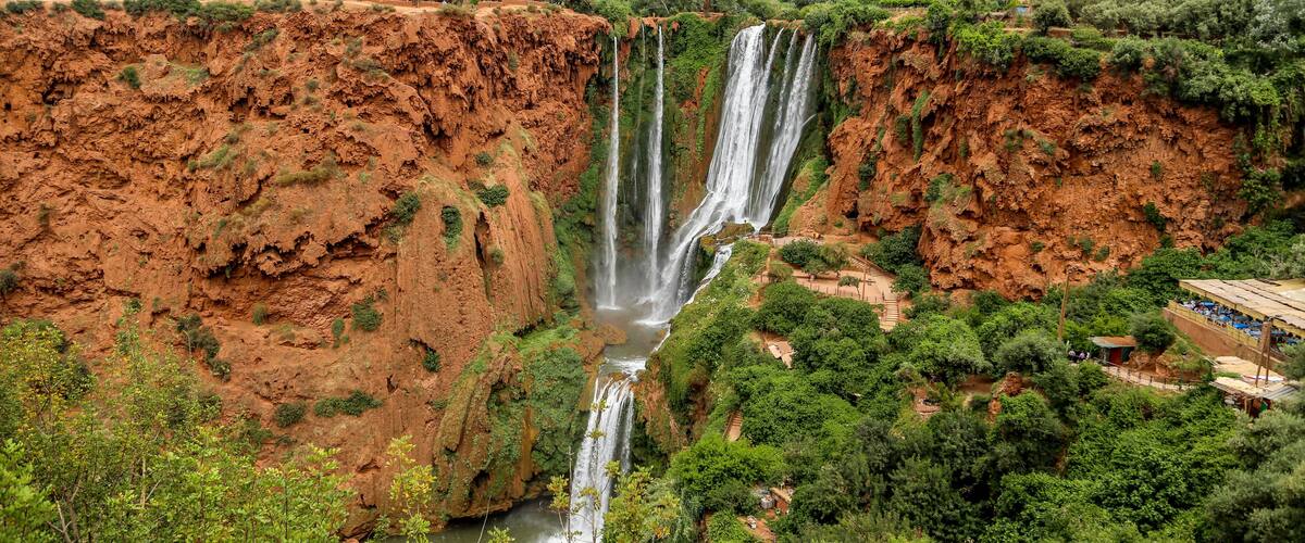 A large waterfall cascading down a steep cliff surrounded by lush greenery and a distant village.