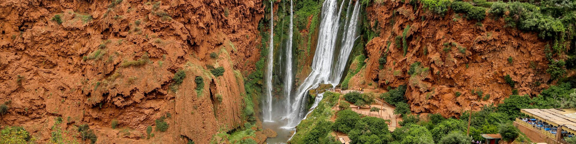 A large waterfall cascading down a steep cliff surrounded by lush greenery and a distant village.