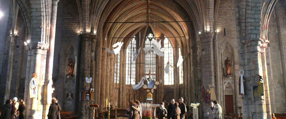 A cathedral interior with high vaulted ceilings, arched windows, and statues.