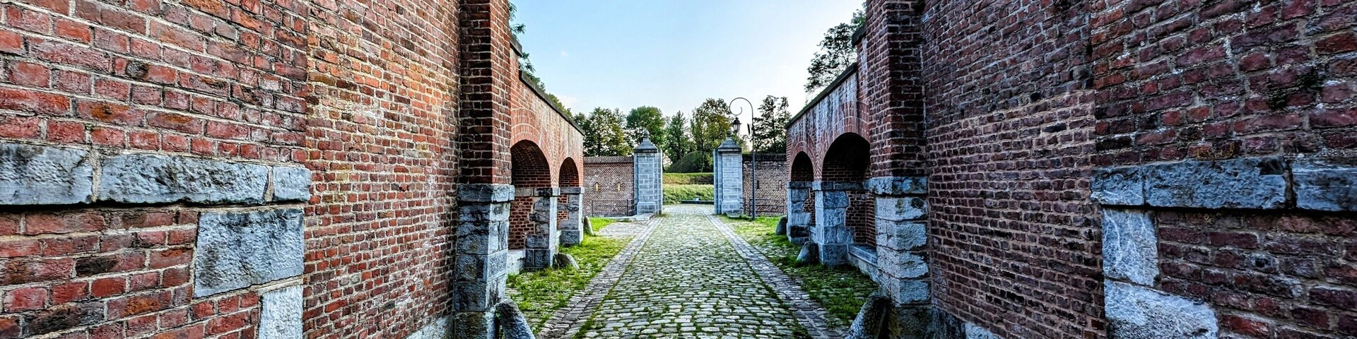 A cobblestone pathway flanked by red brick walls with stone pillars and arched openings.