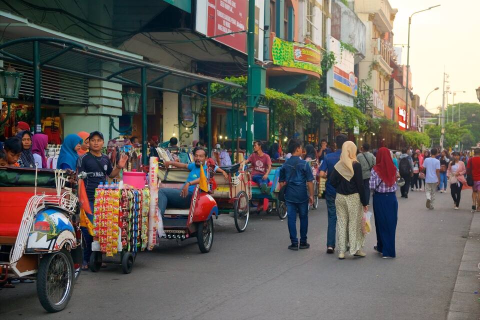 A busy street with people, a tuk-tuk, and various shops.