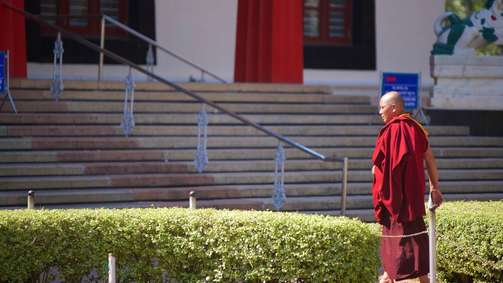 A monk in traditional attire walking past a staircase with red accents and a blue sign.