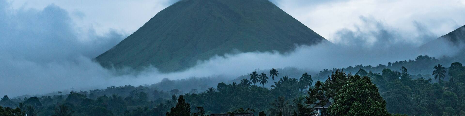 A mountain partially obscured by clouds, surrounded by dense tropical vegetation.