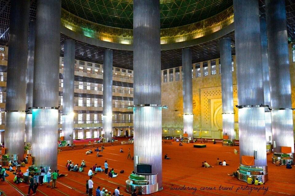 Un amplio espacio interior con altas columnas metálicas y un muro estampado al fondo.