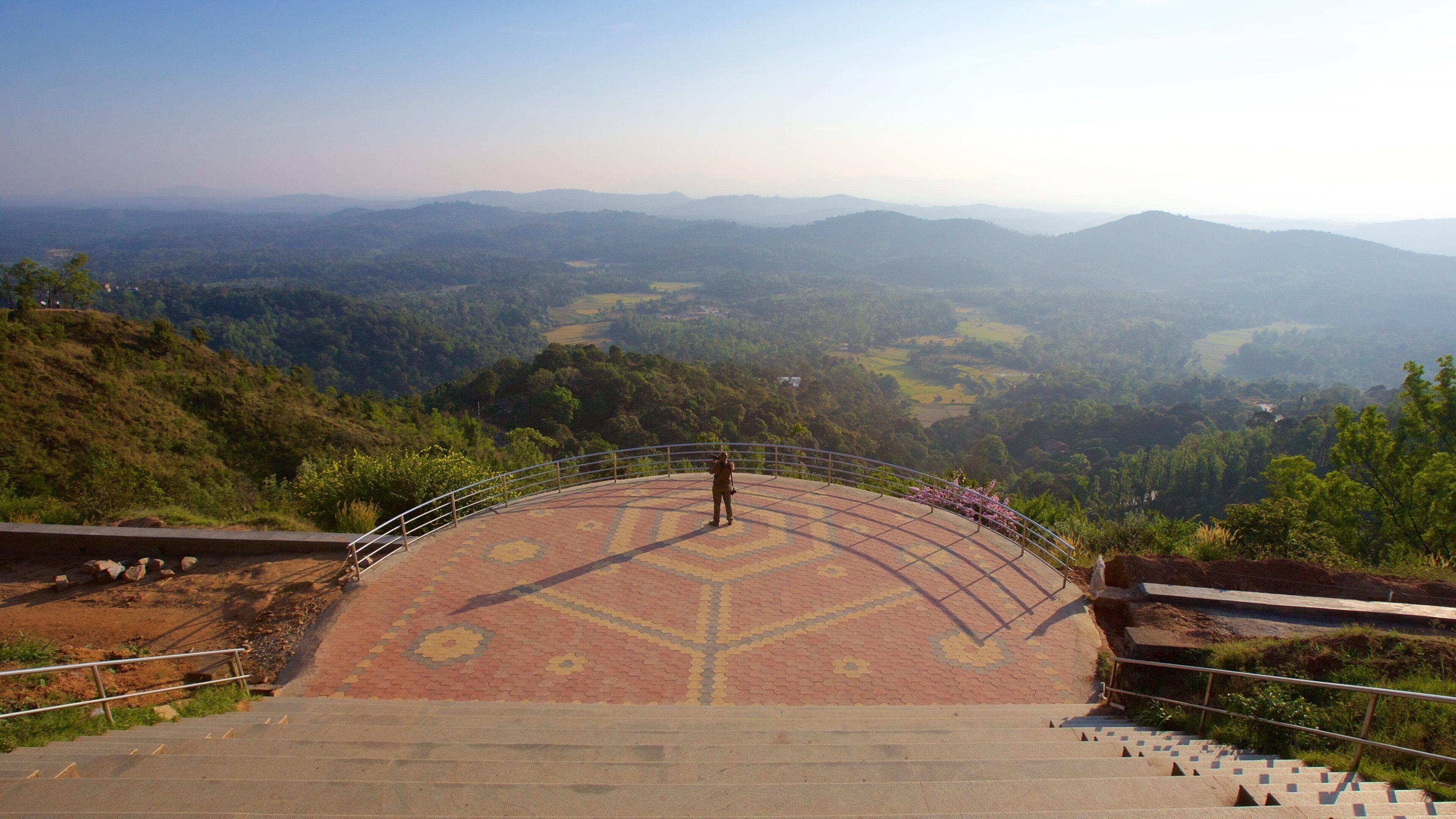 Una persona de pie sobre una plataforma con diseño, con vistas a un valle y montañas distantes.