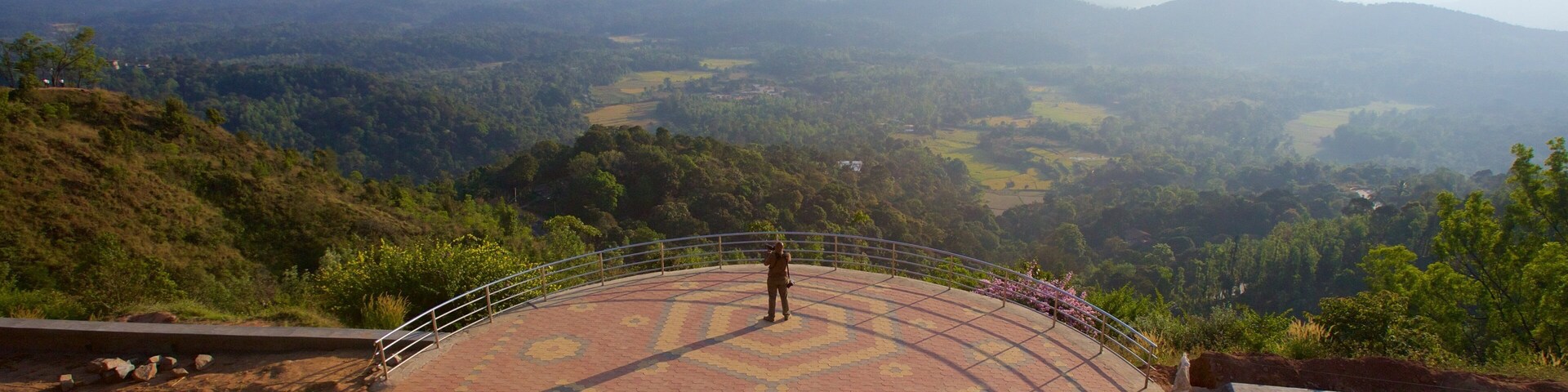 Una persona de pie sobre una plataforma con diseño, con vistas a un valle y montañas distantes.