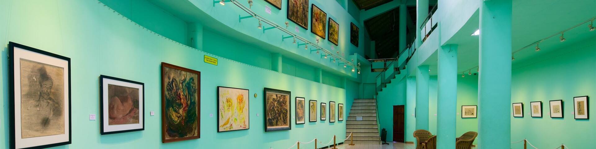 A gallery with art on teal walls and wooden floors.