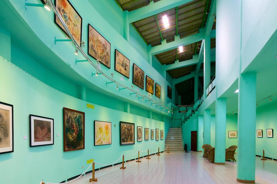 A gallery with art on teal walls and wooden floors.