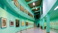 A gallery with art on teal walls and wooden floors.