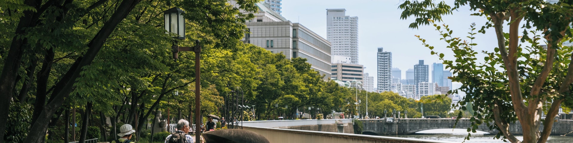 A park with a bridge, trees, and buildings in the background.