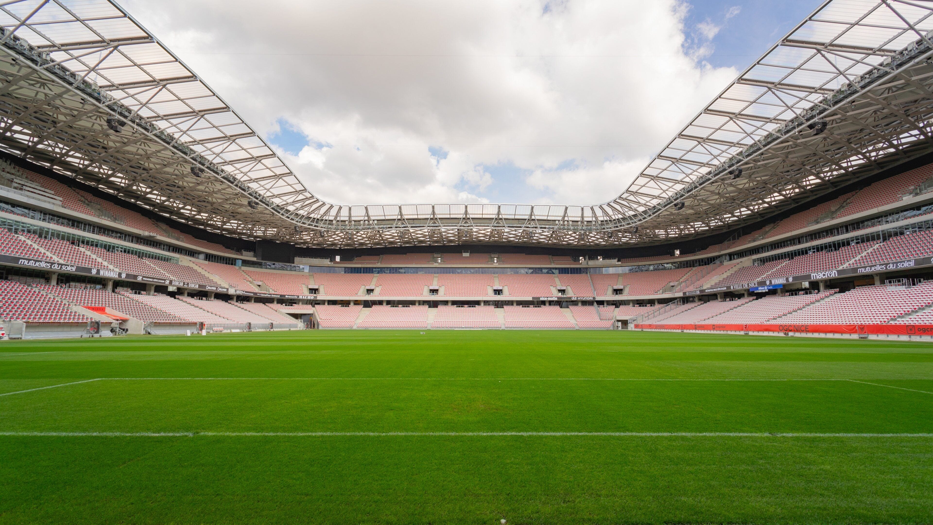 Ein großes, leeres Stadion mit einem grünen Spielfeld und einer Metall-Dachkonstruktion.