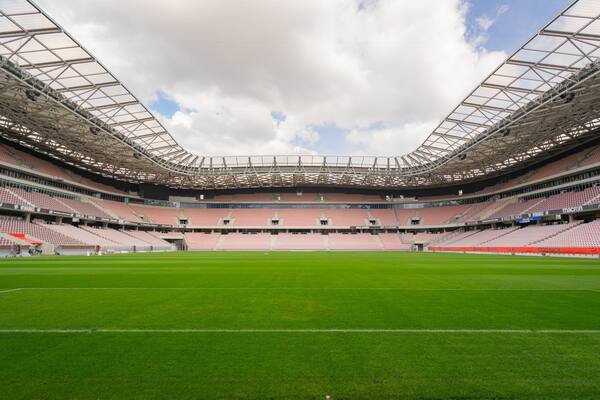 Un grand stade vide, avec un terrain verdoyant et une structure de toit en métal.