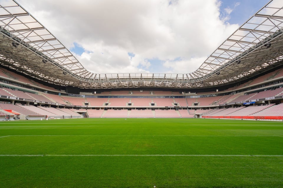 Un grand stade vide, avec un terrain verdoyant et une structure de toit en métal.