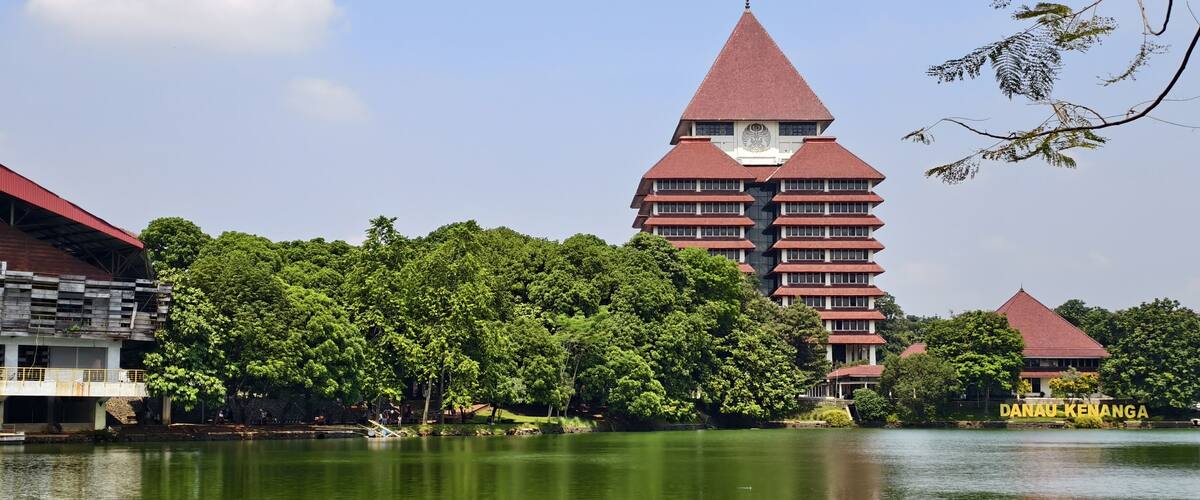 A traditional multi-tiered building with a red roof, surrounded by lush greenery and a calm lake.