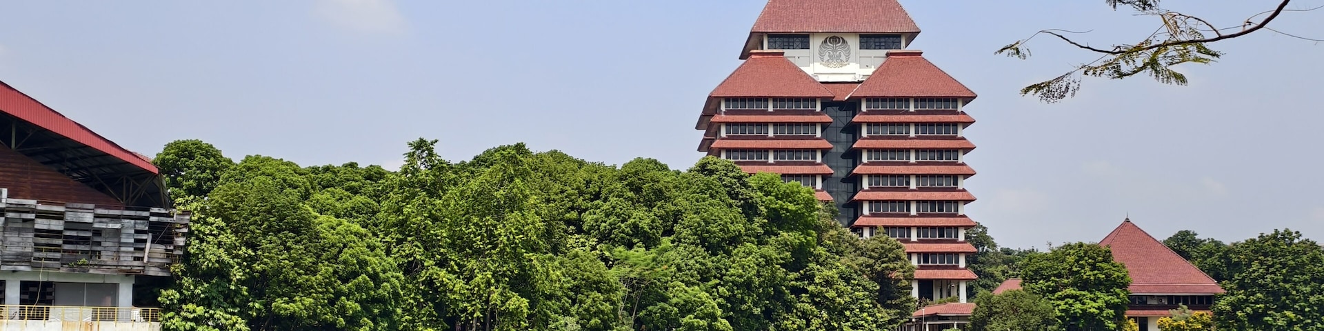 A traditional multi-tiered building with a red roof, surrounded by lush greenery and a calm lake.