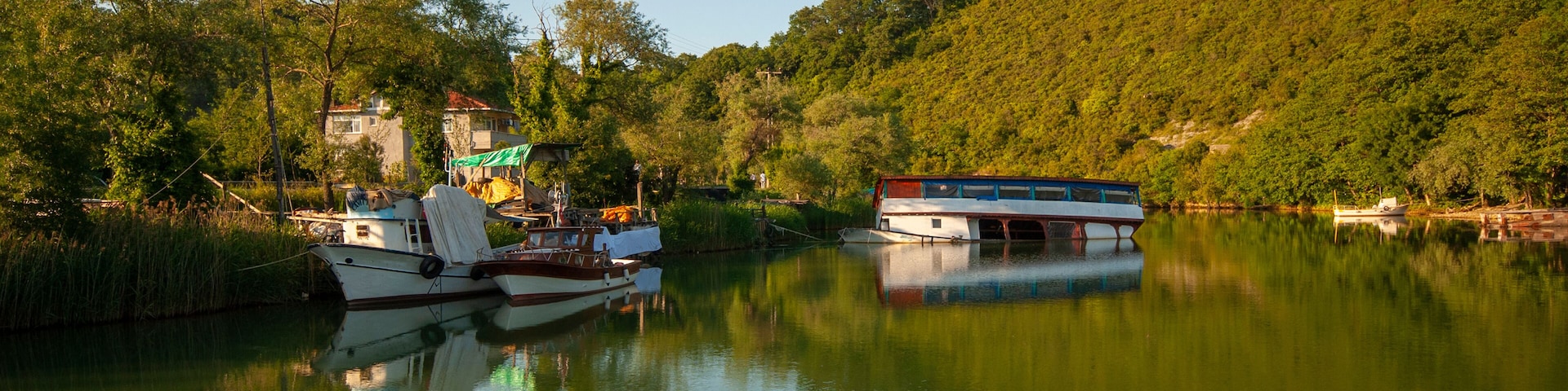Un río tranquilo con barcos, un puente y un cerro cubierto de bosque.