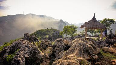 A rocky landscape with a thatched-roof hut and a person standing nearby.