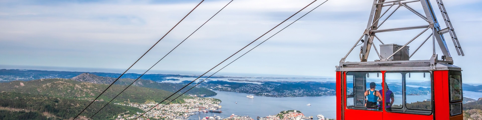 Teleférico sobre uma cidade, com um lago e montanhas ao fundo.