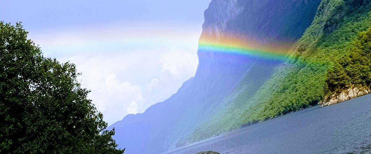 A river with a rainbow, surrounded by lush greenery and mountains.