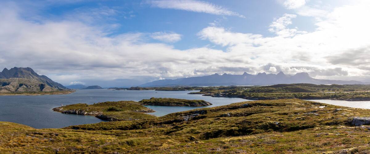A rugged coastline with a prominent mountain peak, a large body of water, and a distant island.