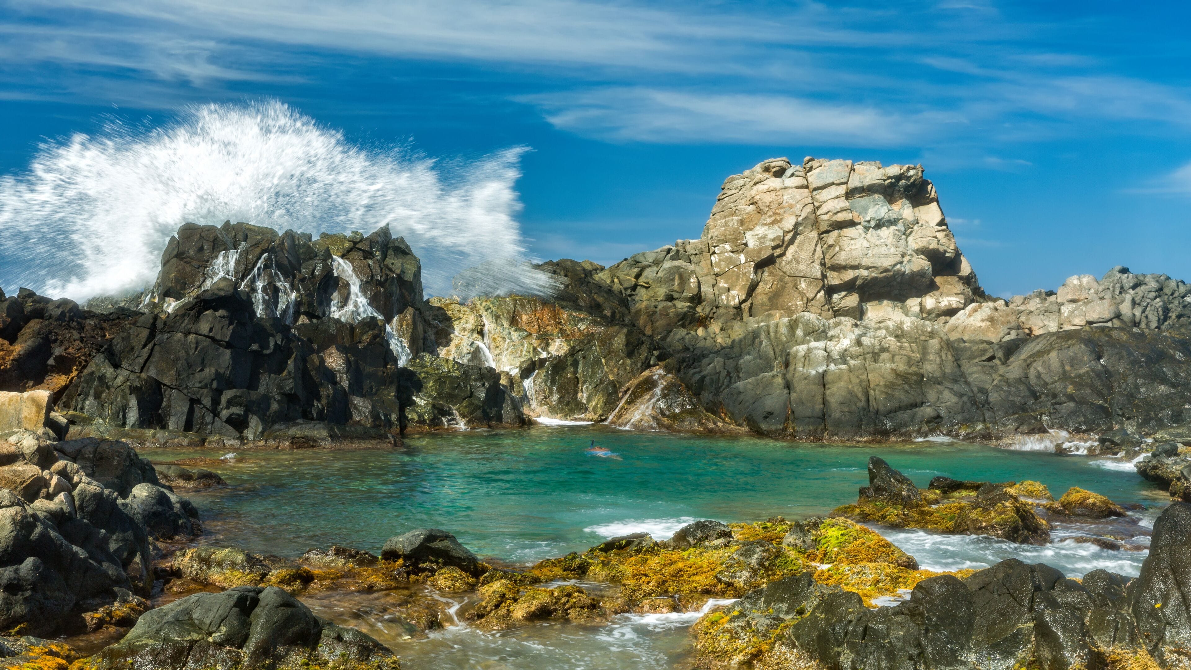 Spectacular wave splashes against the rocks shielding the natural pool (Conchi), a popular tourist attraction, in Aruba.