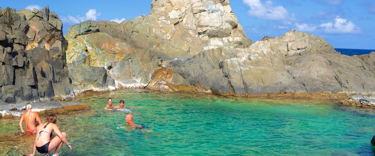 A rocky coastline with clear turquoise water and people swimming.
