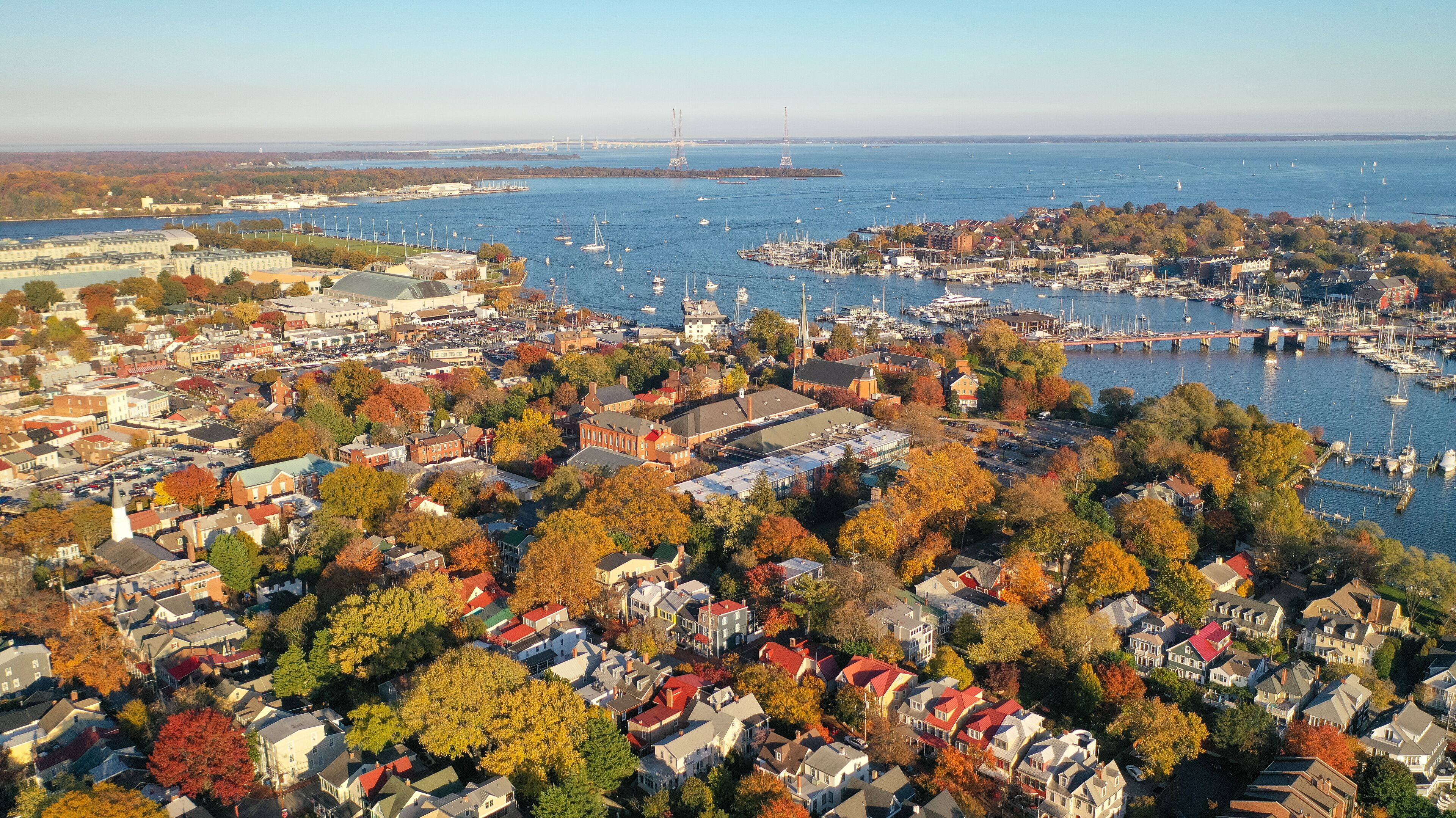 A coastal town with autumn foliage, a marina, and a bridge in the background.