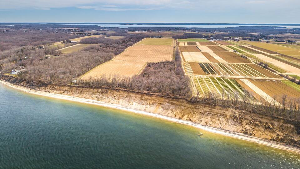 An aerial view of a coastal landscape with fields, a beach, and a body of water.