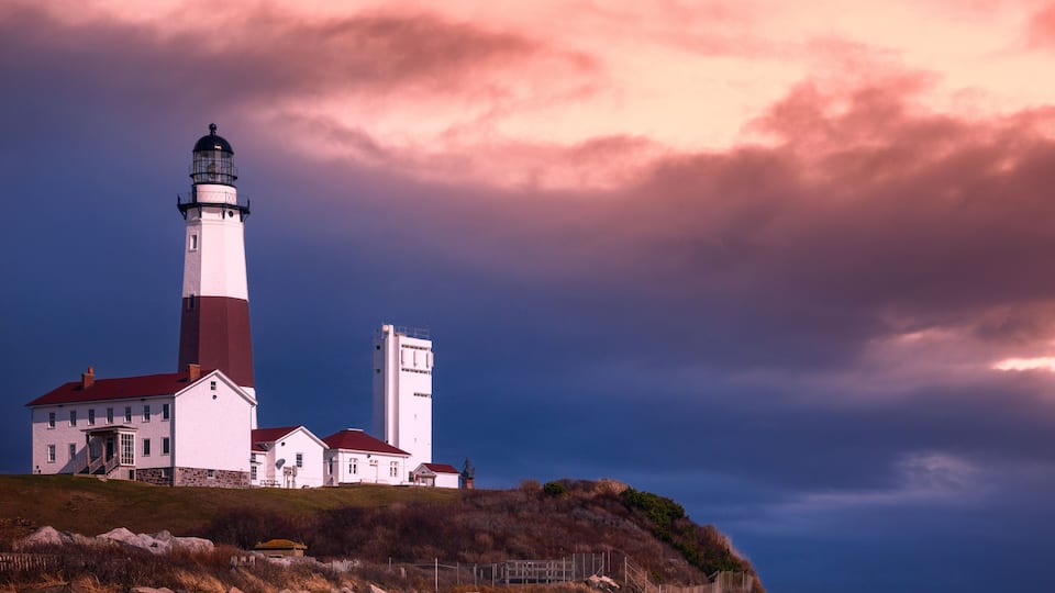 A lighthouse with a red roof, a white building with a red roof, and a rocky shoreline.
