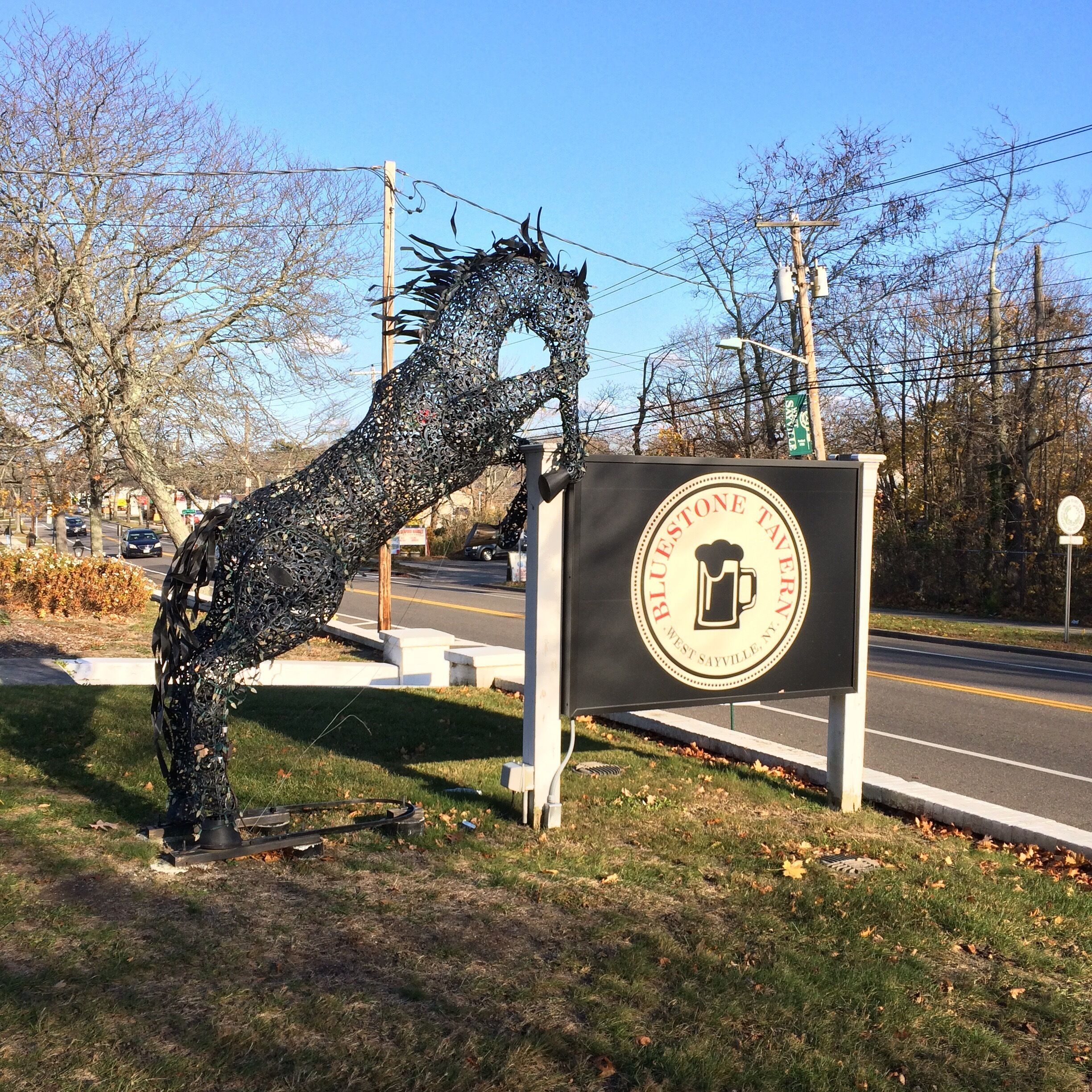 A metal sculpture resembling a horse's head next to a sign for Blue Stone Tavern.