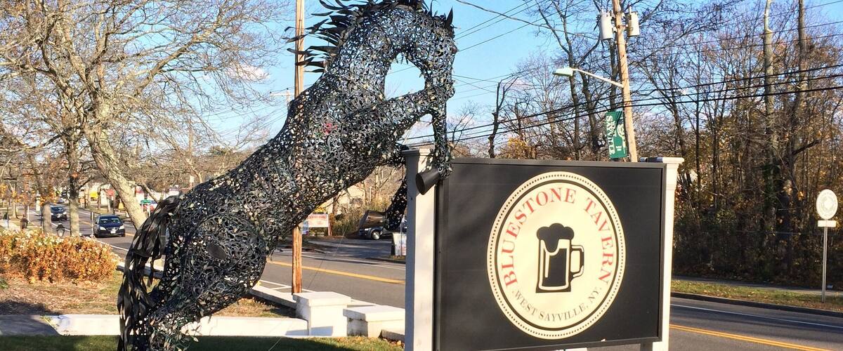 A metal sculpture resembling a horse's head next to a sign for Blue Stone Tavern.