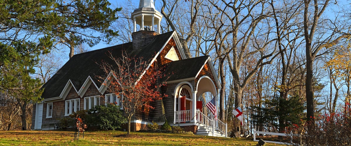 A church with a steeple, surrounded by trees and a grassy lawn.
