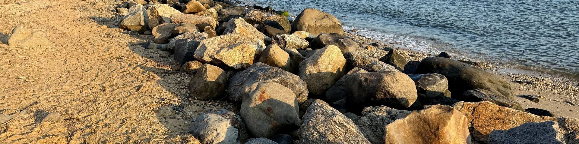 A rocky shoreline with a sandy beach and a clear sky.
