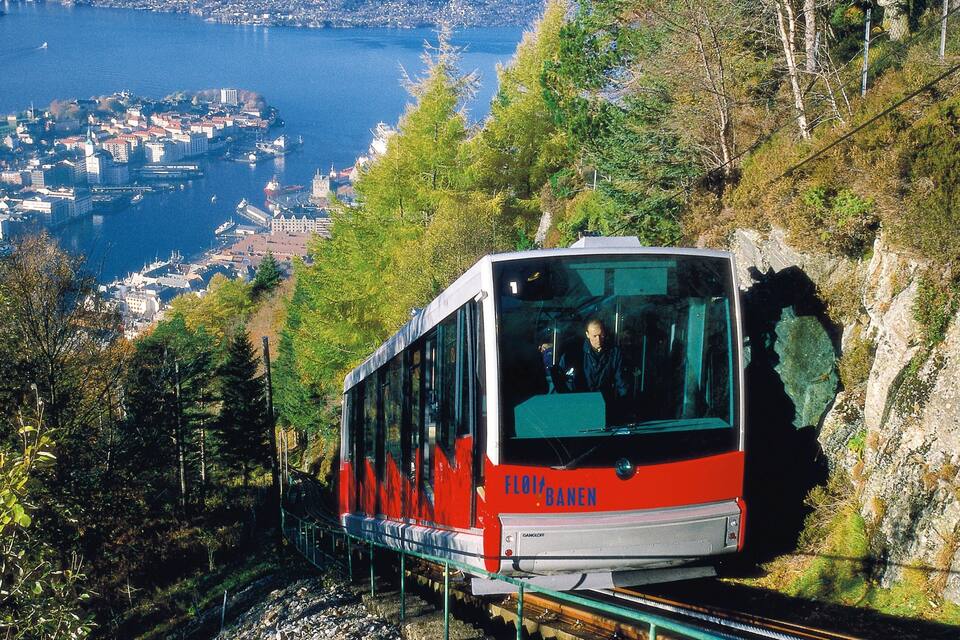 Um trem vermelho e branco em uma linha de montanha, com uma cidade e um lago ao fundo.