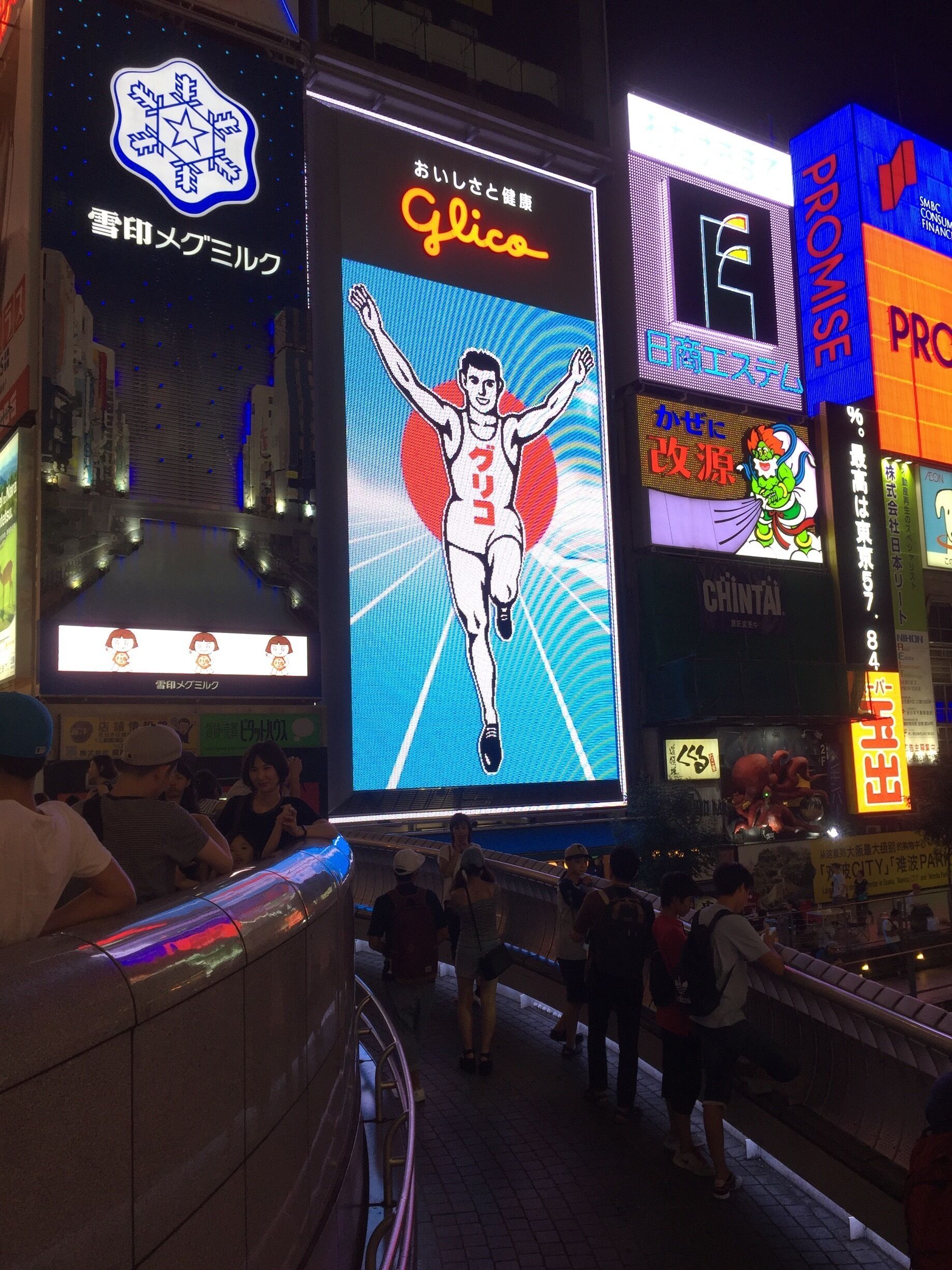 Une rue animée en milieu urbain, bordée de panneaux publicitaires et d’enseignes lumineuses.