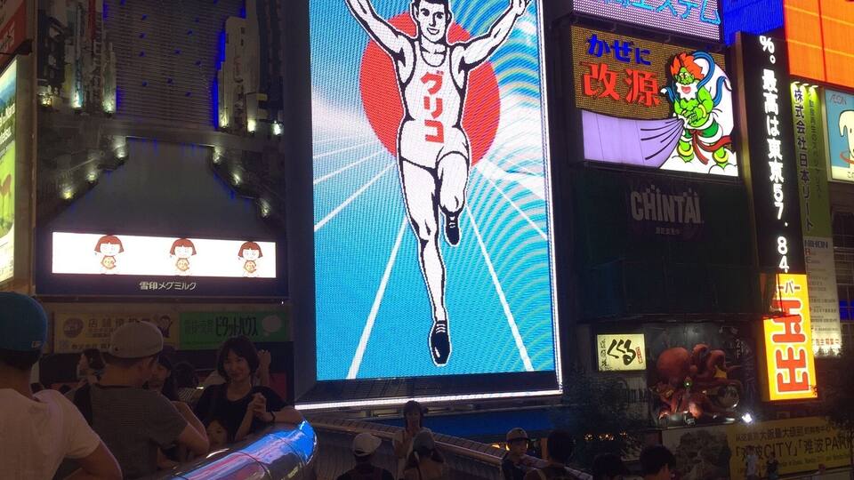 Une rue animée en milieu urbain, bordée de panneaux publicitaires et d’enseignes lumineuses.